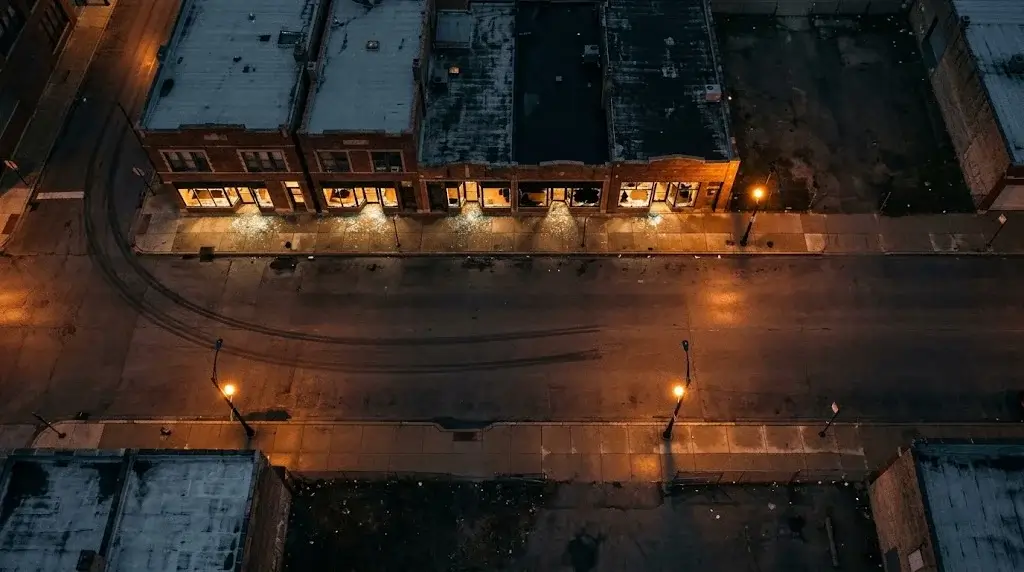 Aerial night view of a Chicago commercial block with every storefront window shattered and glowing