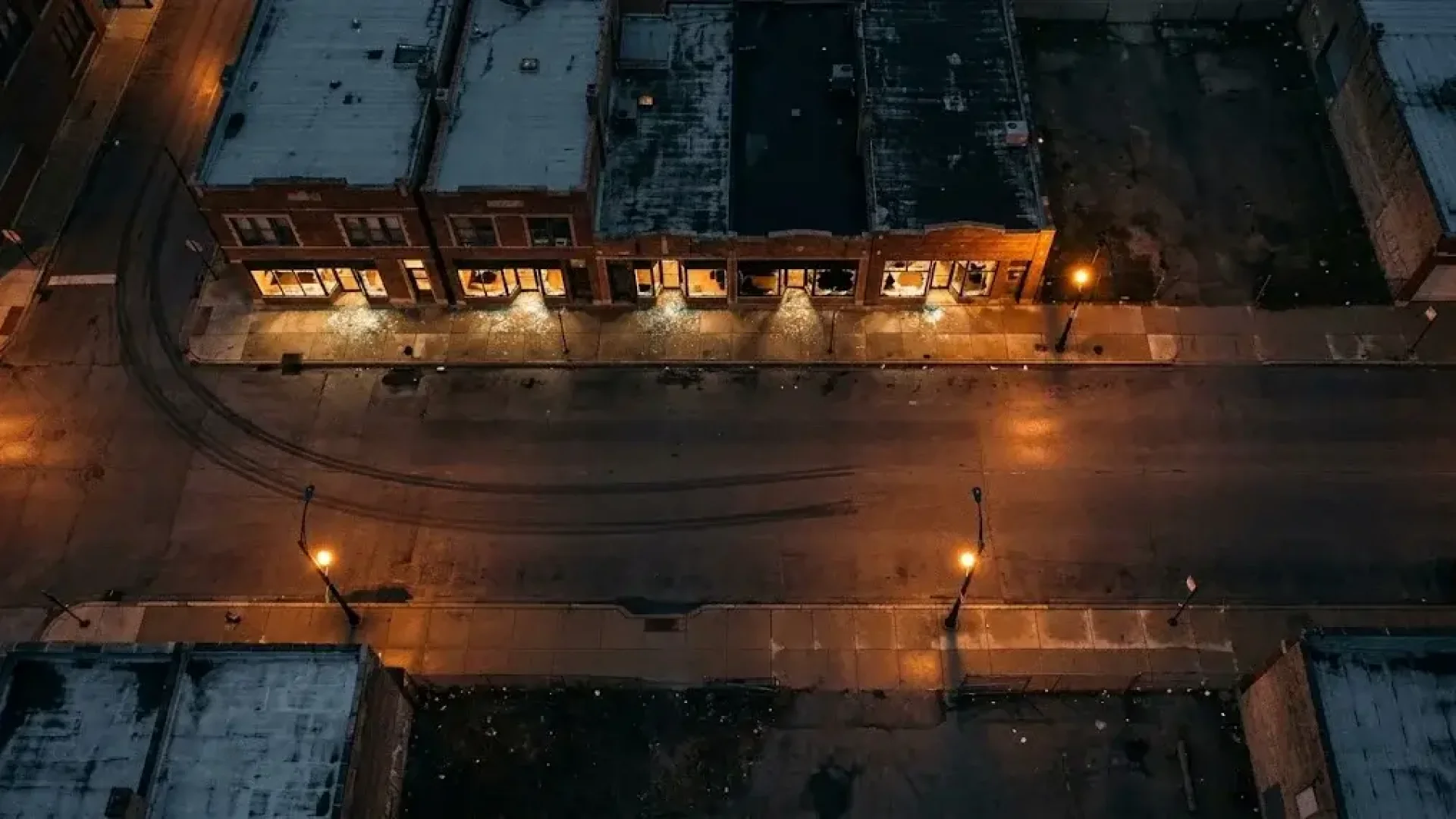 Aerial night view of a Chicago commercial block with every storefront window shattered and glowing